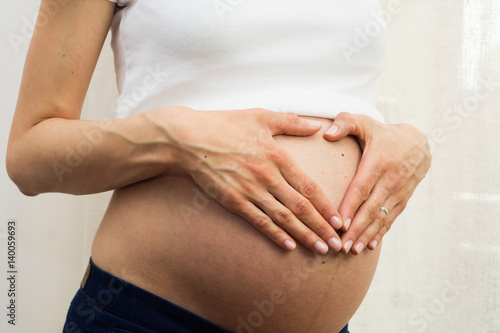 Pregnant woman touching her belly with hands.