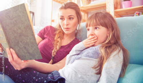 Mother and daughter sitting on sofa and reading book together