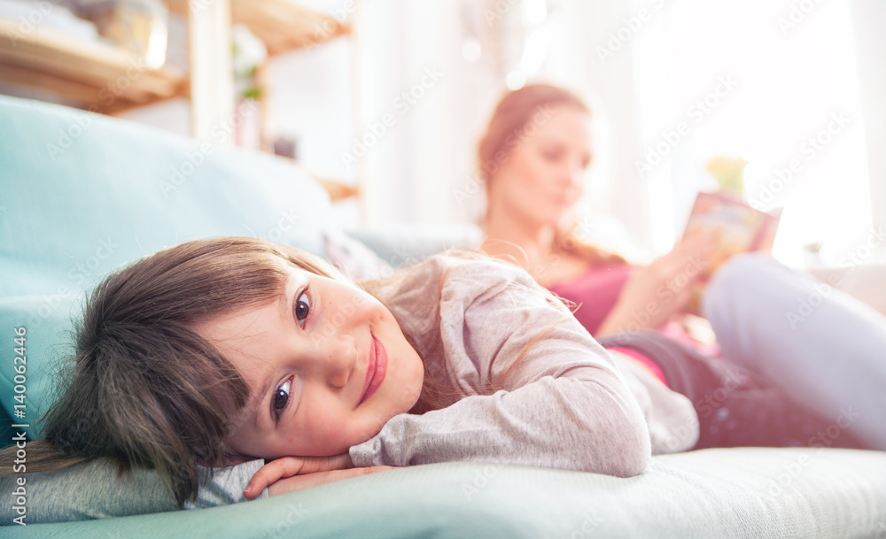 Mother and daughter sitting on sofa and reading book Mother and daughter sitting on sofa and reading book