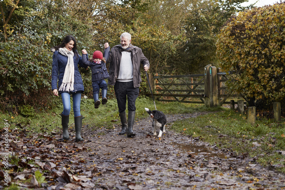 Multi Generation Family Take Dog For Walk In Fall Landscape