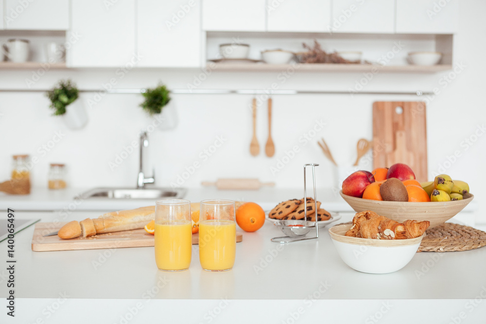 Appetizing Sweet Orange Juice and Two Drinking Glasses standing on a white table in the kitchen for a breackfest. Healthy light meals for breakfast Appetizing Sweet Orange Juice and Two Drinking Glasses standing on a white table in the kitchen for a breackfest. Healthy light meals for breakfast