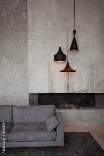 Gray velour sofa in a dark room the bright light from eternal light, and artificial fireplace. Interior loft with concrete walls