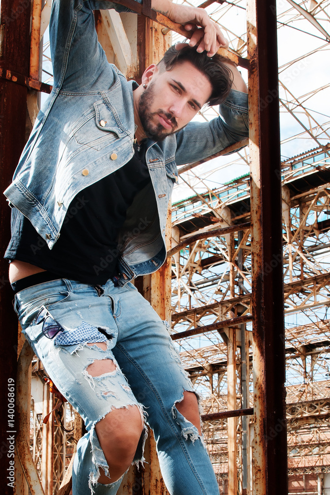 young man on a ladder with denim jacket, black shirt and pants of low waist  jeans. metropolitan background. Sunglasses in one hand. a hand through his  hair. Stock Photo | Adobe Stock