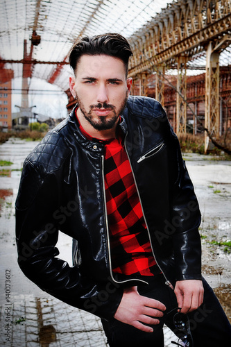 young trendy man with leather jacket, red shirt and black pants with low  waist. metropolitan background. Sun glasses in hand Stock Photo | Adobe  Stock