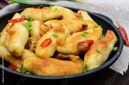 Popular traditional Czech, Hungarian, German dish: potato knedli (dumplings) with slices of fried bacon, spicy red pepper and green onions. Serving on a cast iron pan.
