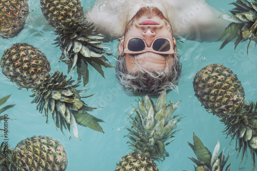 Young man in swimming pool surrounded by pineapples photo