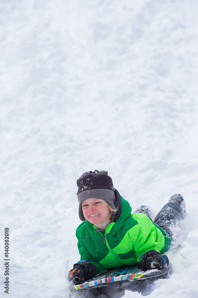 Boy riding a sled tobogganing in the snow Boy riding a sled tobogganing in the snow