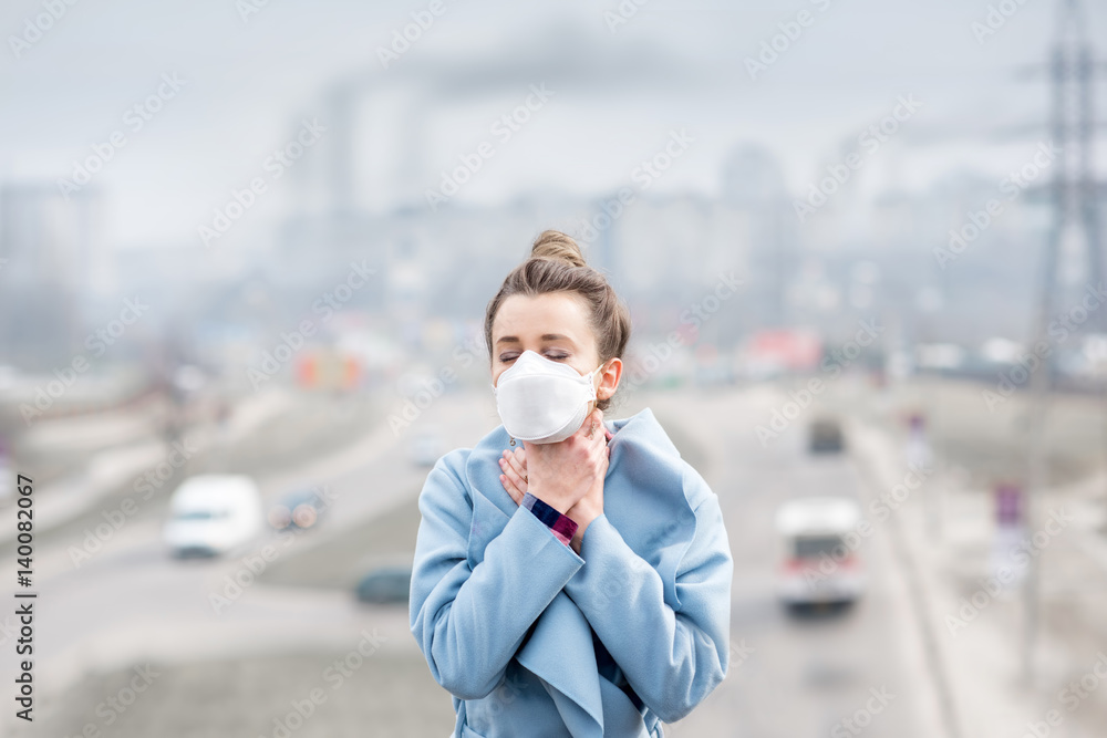Young woman in protective mask feeling bad in the city with air pollution from traffic and manufacturing. Smog concept