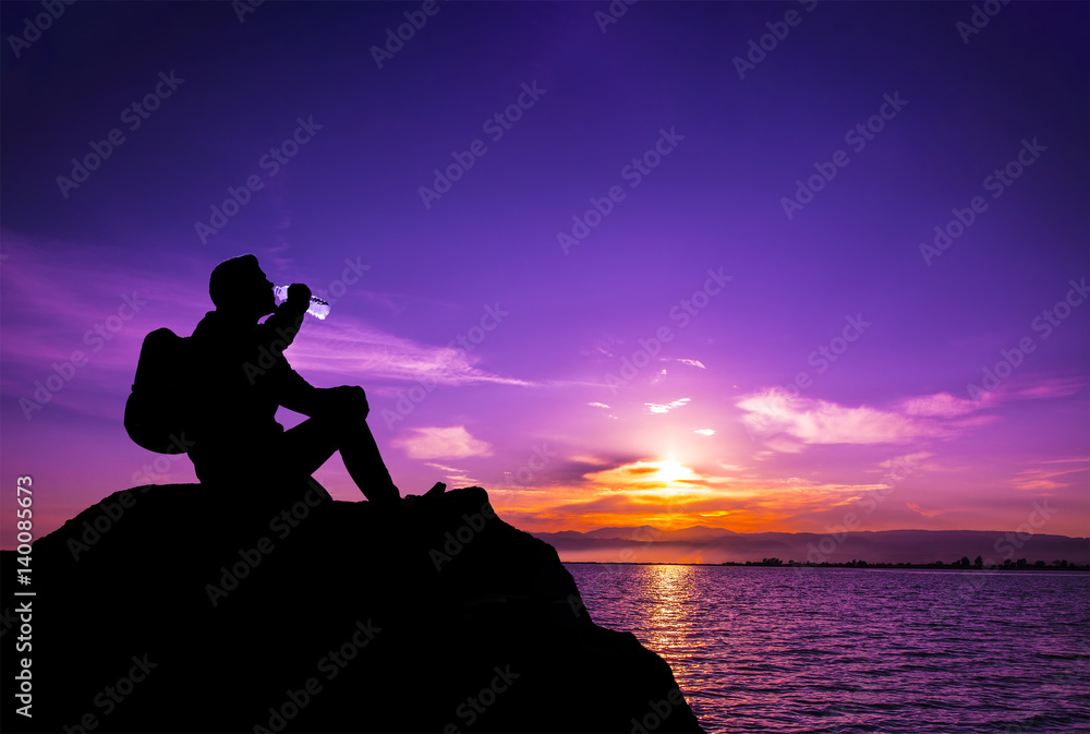 young man silhouette drinking water on the stone at sunset ,Silhouette concept