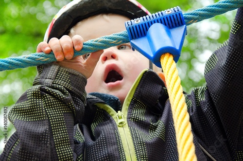 Little boy wearing helmet is climbing on the jungle gym. He is afraid of falling and screaming for help. Child concept.