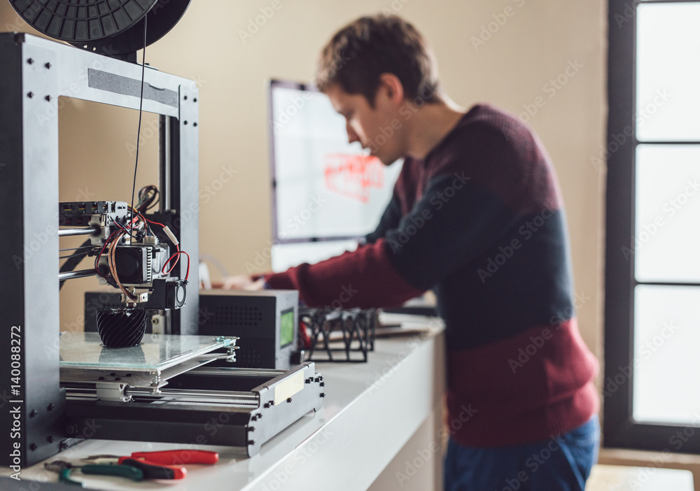 Young Caucasian man graphic designer working next to 3d printer. Young Caucasian man graphic designer working next to 3d printer.
