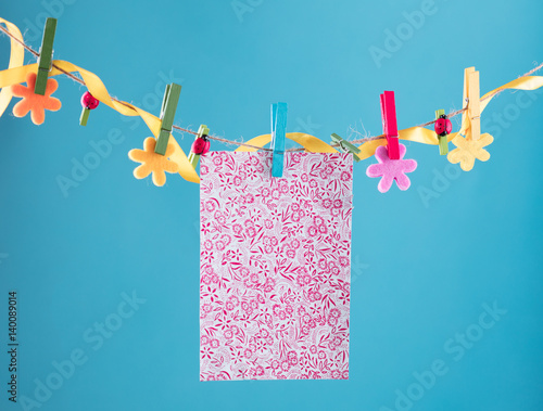 Blank card pinned on clothesline. Copy space for wordings. Pinned with flower pins. Blue, orange background. High resolution photo.