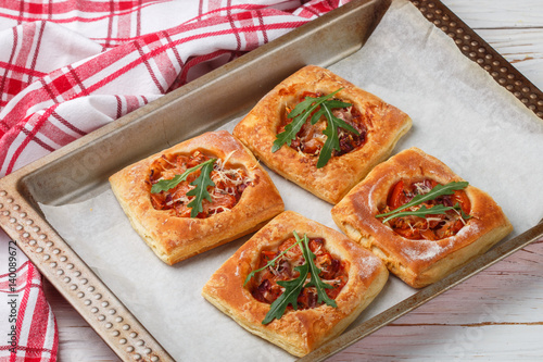 Homemade pies of puff pastry with tomato, red onion, cheese, arugula and herbs . Selective focus