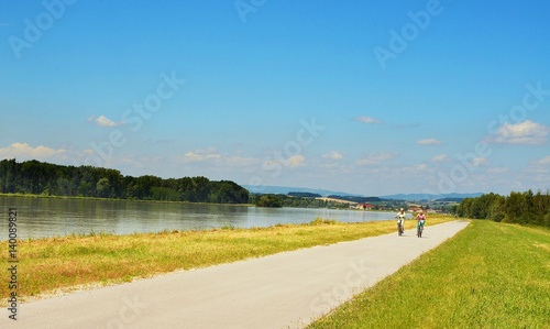Well known Danube cycle trail running along the Danube river in Austria and two cyclists ride along cycle path during beautiful weather in the summer.