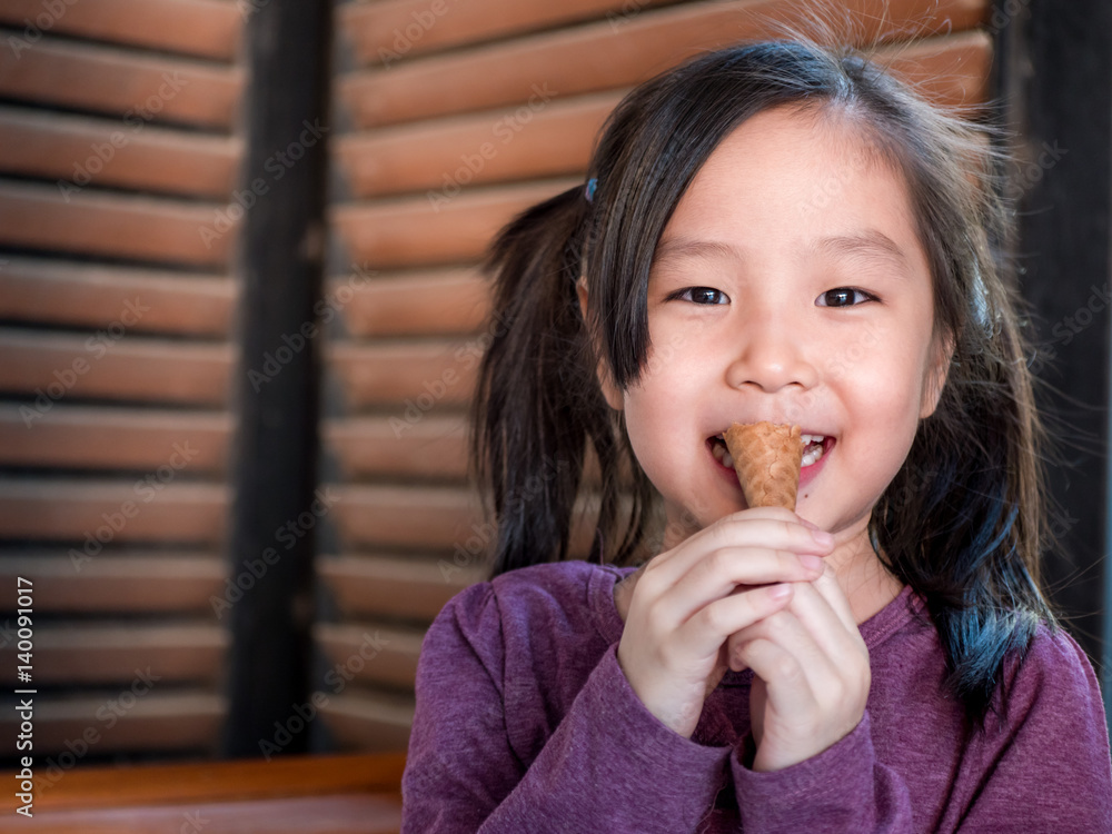 Little Asian girl eating ice cream, wood shade stripes background Little Asian girl eating ice cream, wood shade stripes background