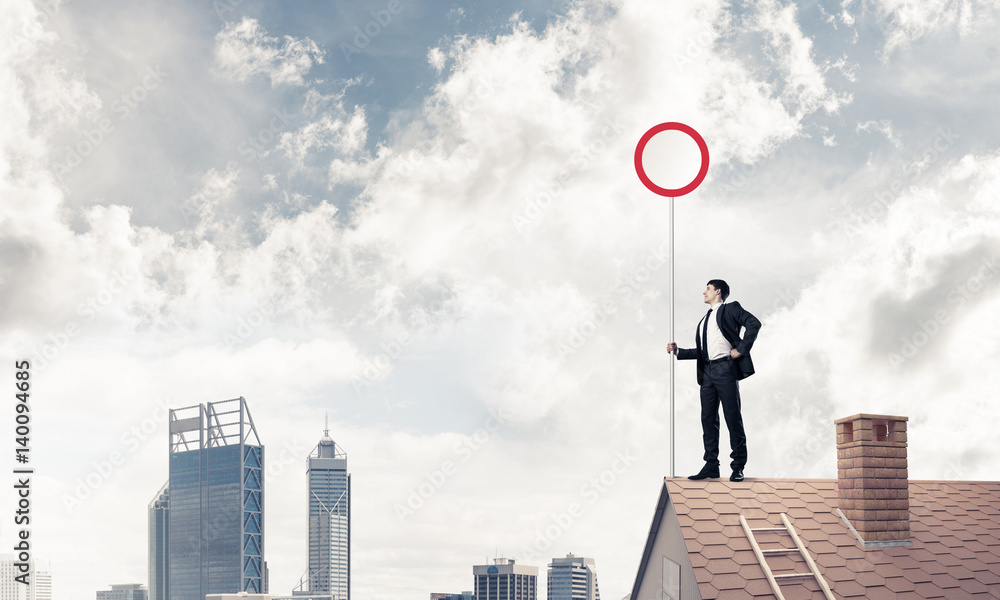 Caucasian businessman on brick house roof showing stop road sign Caucasian businessman on brick house roof showing stop road sign