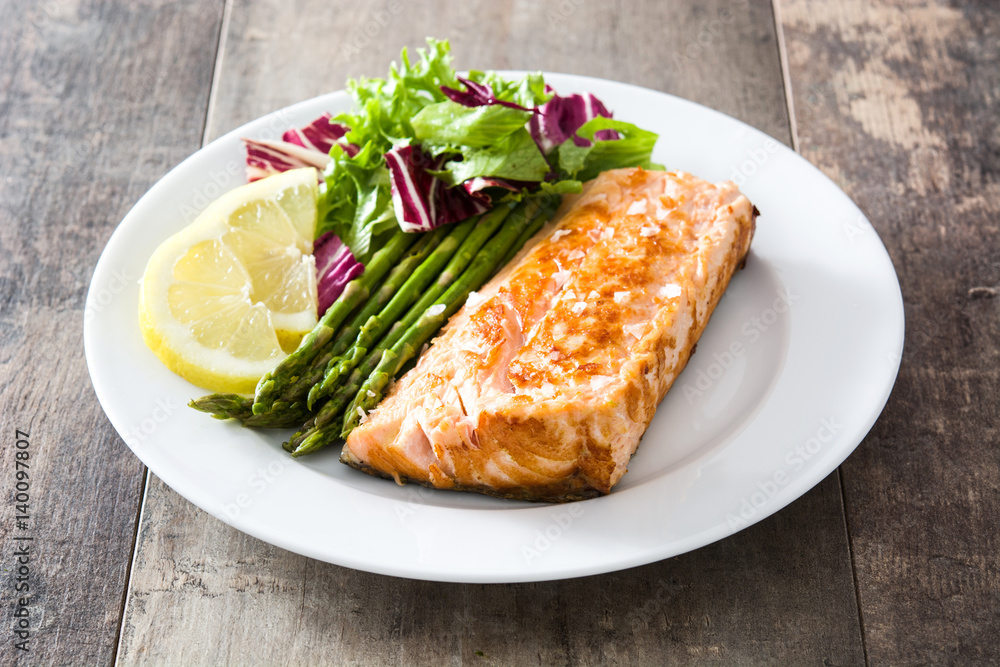 Grilled salmon fillet with asparagus and salad in plate on wooden table
