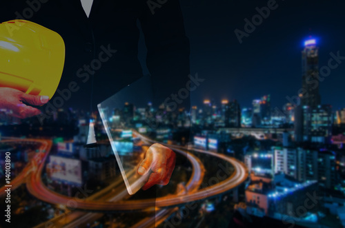 double exposure of professional engineer hold in hand yellow safety helmet and laptop business and industrial concept on night city background  blue color tone effect.