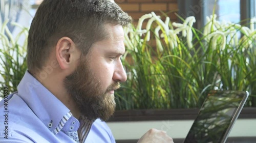 Businessman browsing tablet computer, profile, in cafe, very close steadicam