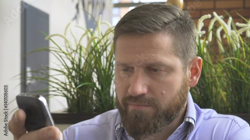 Businessman brows smartphone, look at camera, in cafe, close steadycam portrait