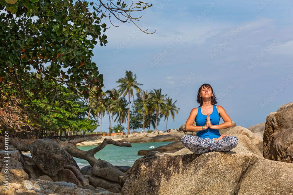 Woman sitting on the beach and doing yoga.