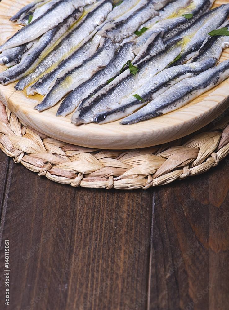 Exquisite marinated anchovies with olive oil and vinegar on brown wooden table. Vertical shoot.