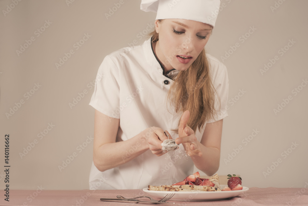 woman chef is spreading powdered sugar on a strawberry crepe woman chef is spreading powdered sugar on a strawberry crepe