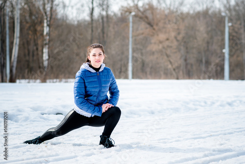 A beautiful young girl is engaged in stretching and gymnastics in the winter forest, on the sports field. Concept photo of a healthy lifestyle © markhipov