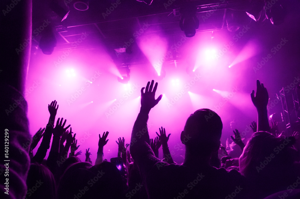 Raised hands of fans during a concert on the background of purple rays of light