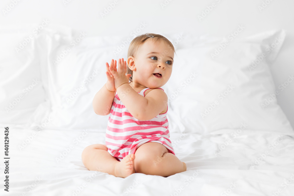 baby girl sitting on a white bed clapping her hands baby girl sitting on a white bed clapping her hands