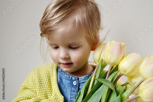 Beautiful little girl holding a bouquet of yellow tulips. Mother's day