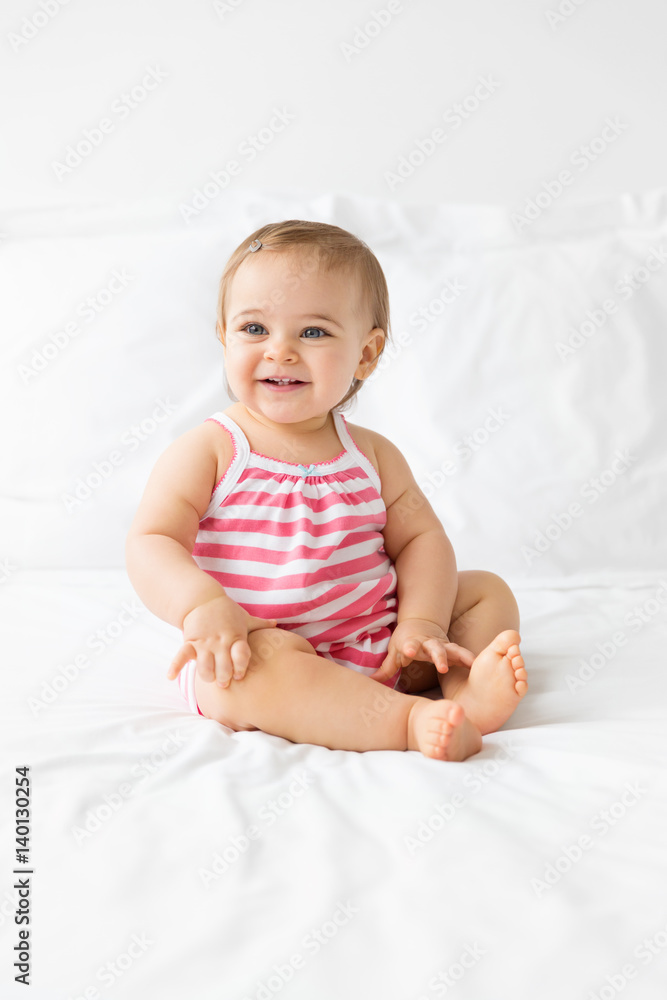 smiling baby sitting on a white bed looking away smiling baby sitting on a white bed looking away