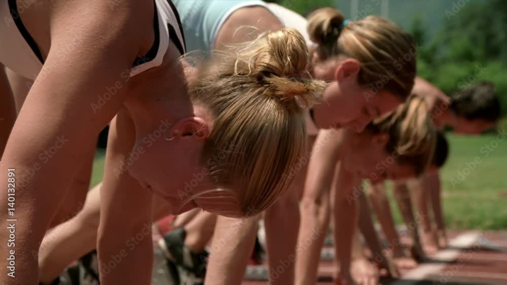 Close-up of women runners lined up at starting blocks and taking off to race