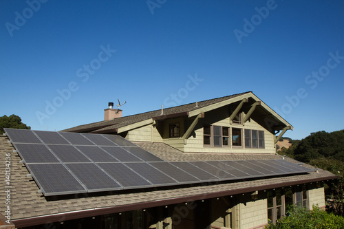 solar panels on roof of house. horizontal orientation, blue sky, gray panels on brown roof.