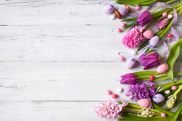 Easter white wooden background with eggs, candy and flowers hyacinths, tulips, space for text greeting