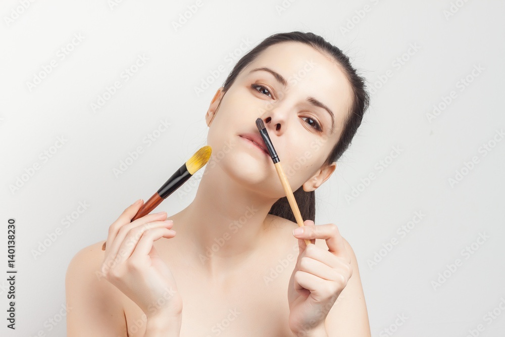 The brunette on a white background with cream on her face, clean face, sponges in hand makeup brush The brunette on a white background with cream on her face, clean face, sponges in hand makeup brush