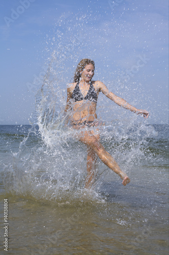Young woman splashing in the shallow water of the sea  blurred motion