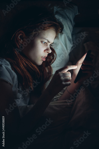 Woman in bed at night with phone in hands, message sms 