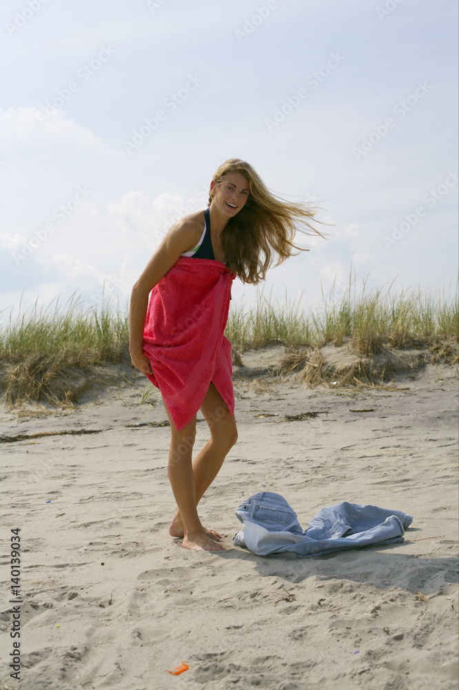 Naklejka premium Young blond woman is changing clothes at the beach