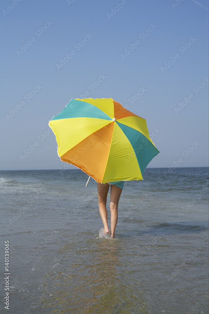 Woman walking in the shallow water of the sea hidden behind a sunshade