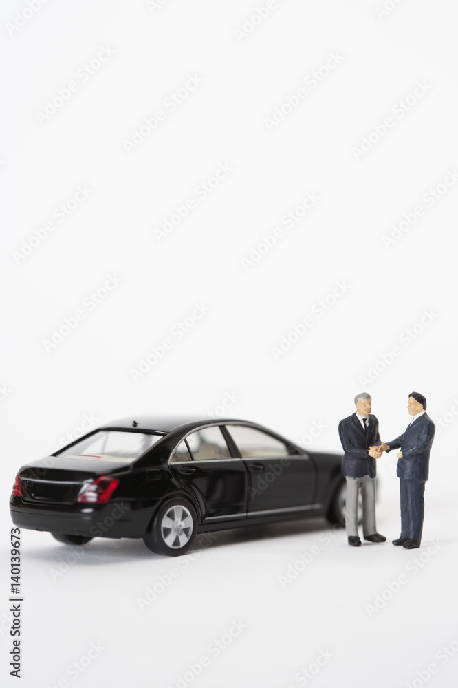 Two businessmen figurines shaking hands in front of a car Two businessmen figurines shaking hands in front of a car
