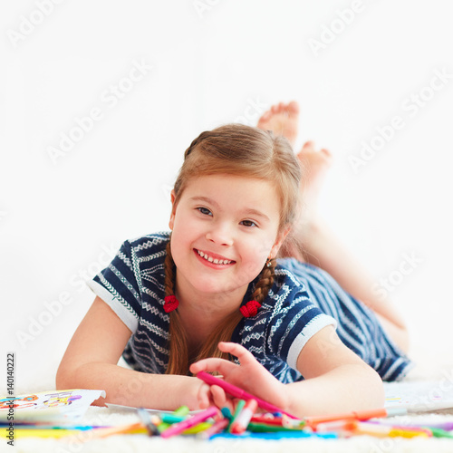 portrait of cute happy girl drawing, while laying on carpet