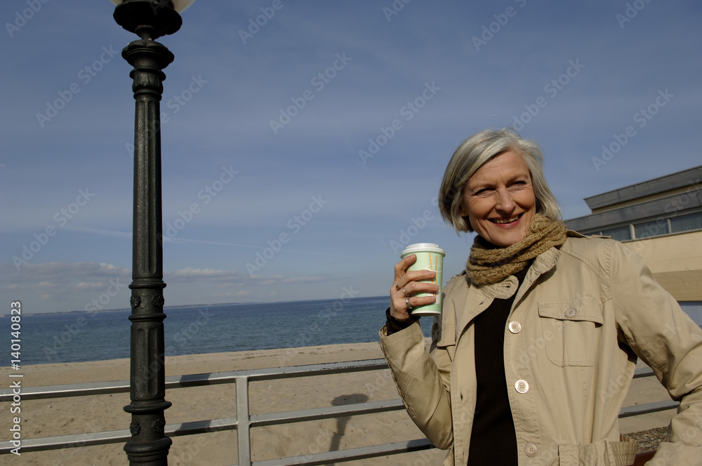 Mature woman at Baltic Sea beach holding a coffee cup