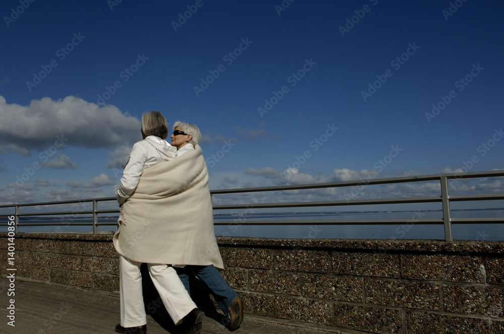 Two mature women wrapped in a blanket walking along the Baltic Sea Two mature women wrapped in a blanket walking along the Baltic Sea