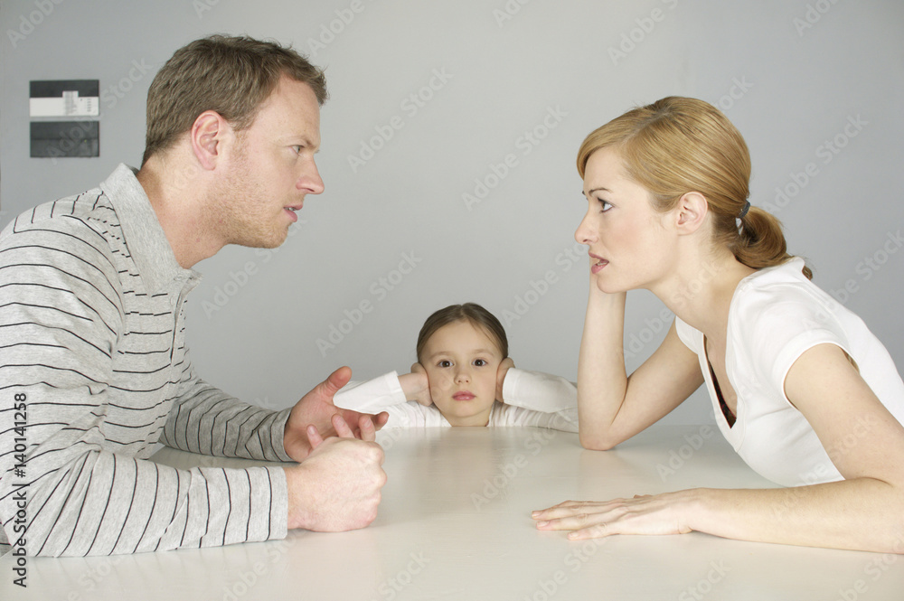 Couple arguing at table, girl in background covering ears with hands Couple arguing at table, girl in background covering ears with hands