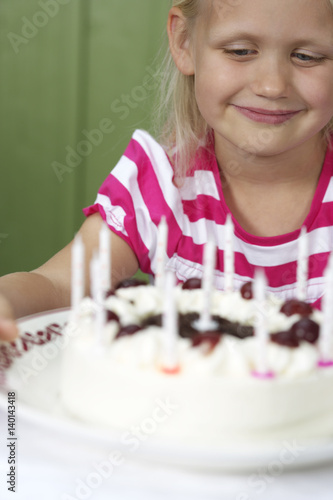 Little blond girl in front of a birthday cake, close-up