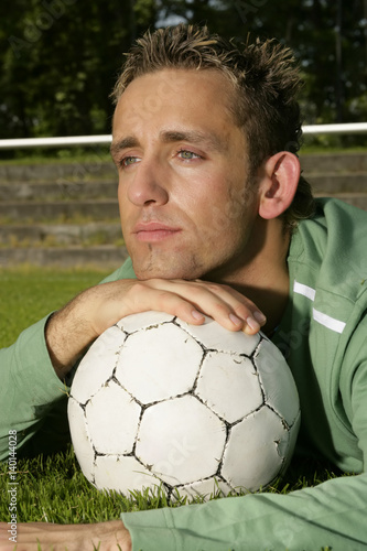 Young man with blond hair with his head resting on a football, close-up © Gudrun
