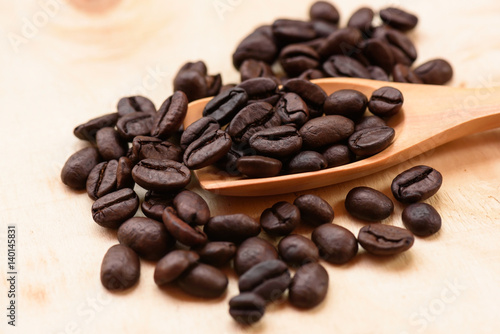 Coffee beans and wooden scoop on wooden background.