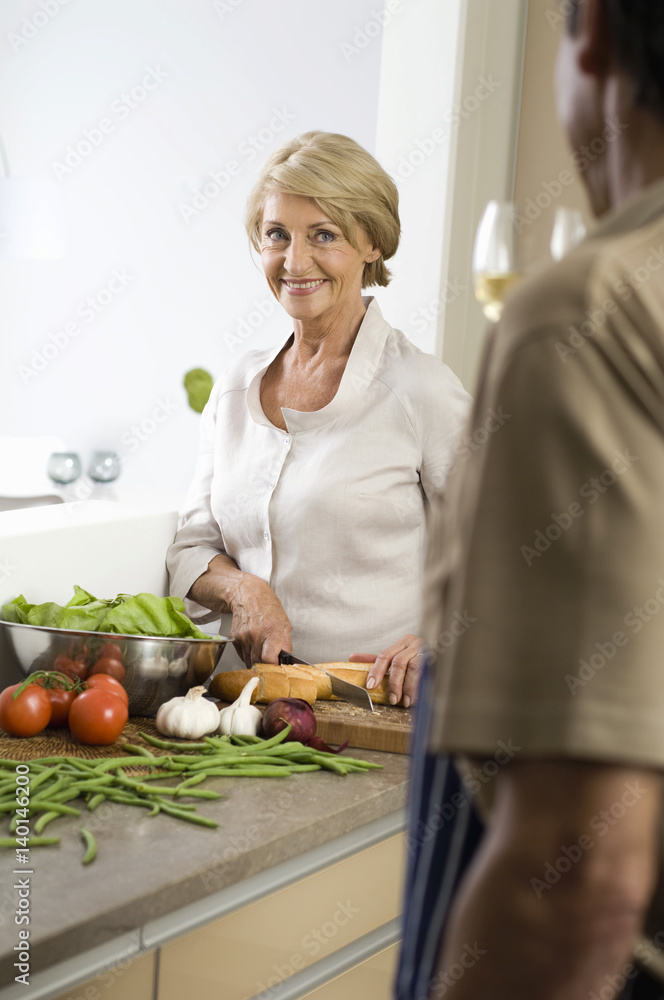 Senior woman cutting baguette, man drinking a glass of white wine