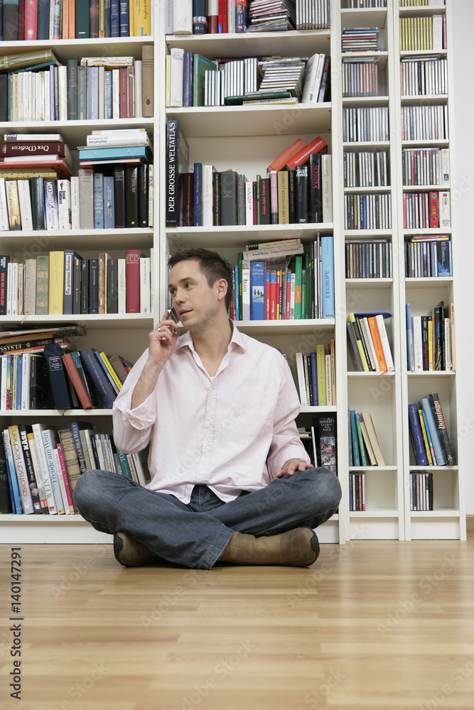Man sitting in front of a shelf and using a mobile phone Man sitting in front of a shelf and using a mobile phone